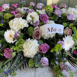 Large floral tribute with pink, lavender, white, and green blooms and a "Mom" card