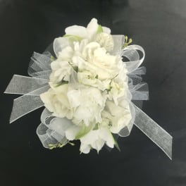 White floral wrist corsage with sheer ribbon on a black background