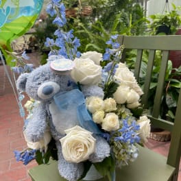 Blue teddy bear with white roses and blue flowers in a vase