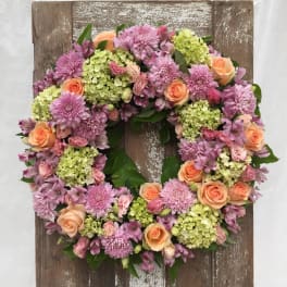 Floral wreath with pink and peach blooms on a rustic wooden board
