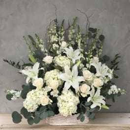 White lilies and cream roses arranged in a basket with greenery