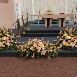 Three pastel floral arrangements on a church altar platform