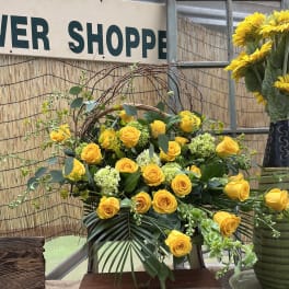 Yellow roses arranged with pale green blooms in a basket display