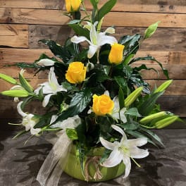 Yellow roses and white lilies arranged in a green vase with a ribbon bow.
