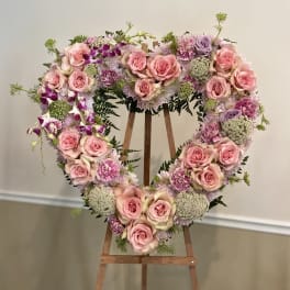 Heart-shaped floral wreath with pink roses and lavender blooms on a wooden easel