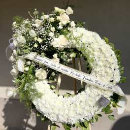 White floral funeral wreath on an easel with a ribbon banner