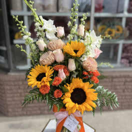 Bouquet of sunflowers, roses, and pale blooms in a glass vase with ribbons
