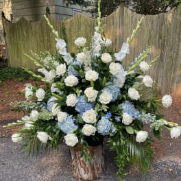 Large white and blue floral arrangement with roses and tall spikes in a wood base