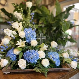 Blue hydrangeas and white roses arranged with a clear cross centerpiece