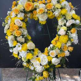 Heart-shaped floral wreath with yellow and white roses and daisies on an easel