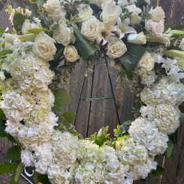 Large white floral wreath on an easel with roses, hydrangeas, and calla lilies
