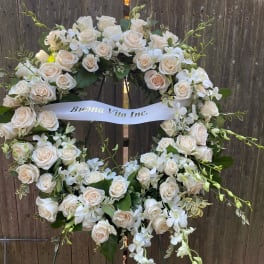 White rose wreath with orchids and a ribbon on a stand