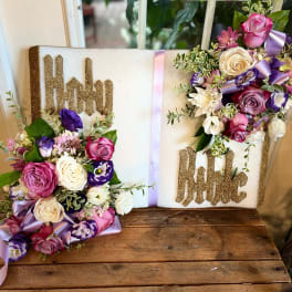 Religious book-style floral tribute with pink, white, and purple blooms on a Holy Bible plaque
