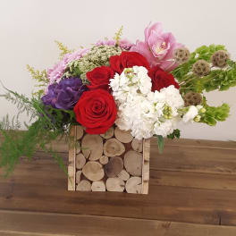 Mixed bouquet of red, white, pink, and purple flowers in a wooden log box