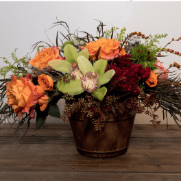 Orange and burgundy floral arrangement in a wooden container