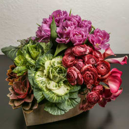 Pink flowers arranged with green ornamental cabbage in a wooden container
