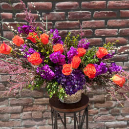 Orange roses and purple flowers in a rustic vase arrangement