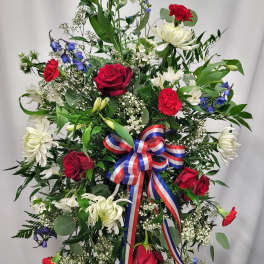 Standing floral spray with red roses, white lilies, and a red-white-blue ribbon