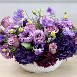 Purple and pink floral arrangement in a white bowl vase