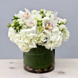 White hydrangeas and orchids arranged in a glass vase