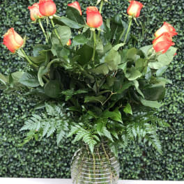 Orange roses arranged in a clear glass vase with fern foliage