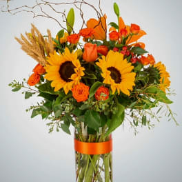 Orange and yellow bouquet with sunflowers and roses in a clear glass vase