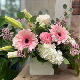 Pink gerbera daisies and roses in a white square vase
