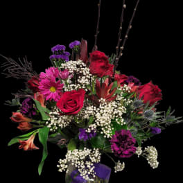 Bouquet of red roses, purple blooms, and white baby's breath in a glass vase