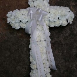 White floral cross with a ribbon bow and hanging memorial ribbons