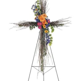 Floral cross arrangement with orange, purple, and pink flowers on a stand