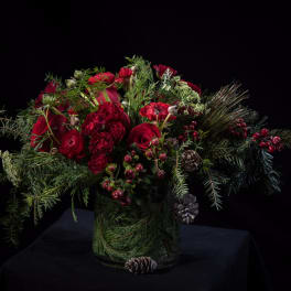 Red roses and winter greenery in a glass vase with pinecones and berries