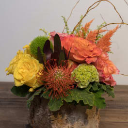Mixed floral arrangement in a rustic bark container with yellow and orange blooms