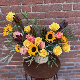 Bouquet of yellow roses and sunflowers in a textured vase