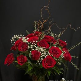 Red roses arranged in a tall glass vase with white baby's breath