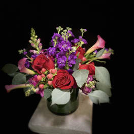 Bouquet of red roses, purple flowers, and pink calla lilies in a glass vase
