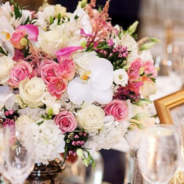 Pink and white floral centerpiece with roses and orchids in a low arrangement