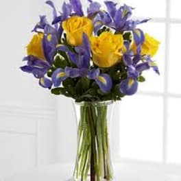 Bouquet of yellow roses and purple irises in a clear glass vase