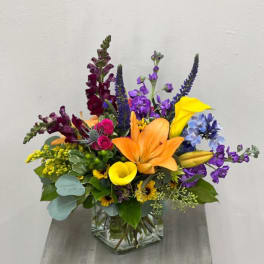 Colorful mixed bouquet in a clear glass vase with lilies, calla lilies, and snapdragons