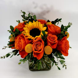 Orange roses and a yellow sunflower in a glass vase