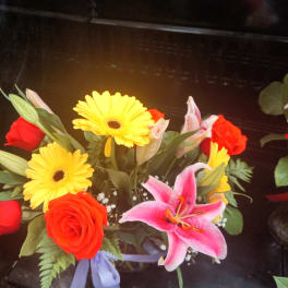 Bouquet with red roses, yellow gerbera daisies, and a pink lily in a vase