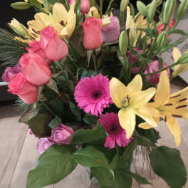 Mixed bouquet of pink roses, yellow lilies, and pink gerbera daisies in a glass vase