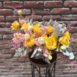 Yellow and pink floral arrangement in a dark vase on a stand