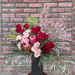 Red and pink floral arrangement in a tall black vase
