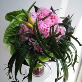 Pink peonies arranged with long dark green leaves in a clear glass vase