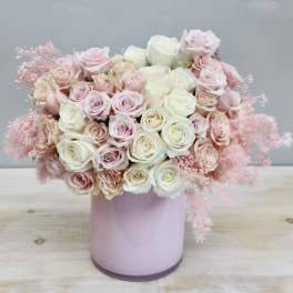 Round arrangement of pale pink and cream roses in a glossy light pink cylinder vase