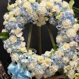 Heart-shaped floral wreath with white roses and blue hydrangeas on an easel