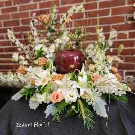Low floral arrangement with white lilies, peach roses, and white daisies in a burgundy vase