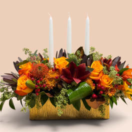 Orange and burgundy floral centerpiece with three white taper candles