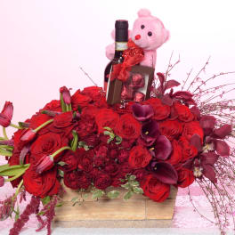 Red rose arrangement with a wine bottle, chocolates, and a pink teddy bear