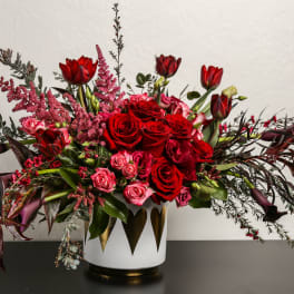 Red roses and tulips in a white vase with dark foliage